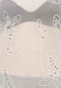 Tessuto in rete trasparente con ricami floreali e paillettes in bianco e argento, caratterizzato da uno sfondo color nude chiaro e una consistenza morbida e fluida.
