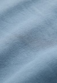 Blødt, lyseblåt stof med en finstrikket tekstur og diskrete folder, der skaber blide skygger over overfladen.