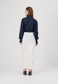 Cămașă albastră cu nasturi, cu mâneci lungi, asociată cu o fustă midi albă, aderentă și sandale negre cu toc gros. Textură de țesătură netedă.