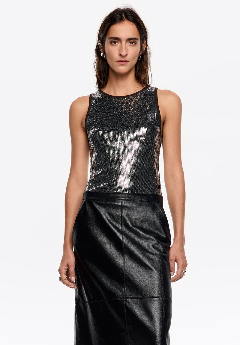 Błyszczący czarny top na ramiączkach z cekinami, o okrągłym dekolcie i bez rękawów, zestawiony z długą czarną spódnicą z eko skóry o gładkiej fakturze.