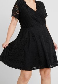 Svart spetsklänning med korta ärmar, v-ringning och utställd kjol. Har ett blommigt spetsmönster och en figurnära midja för en smickrande siluett.