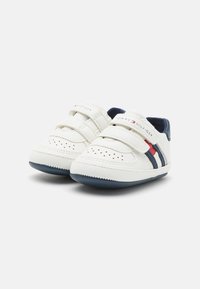 Biele tenisky s námorníckymi akcentmi, suchými zipsami, perforovaným dizajnom a logom Tommy Hilfiger na boku. Gumová podrážka pre lepšiu priľnavosť.