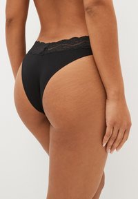 Mustast puuvillasest stringidest aluspesu pitsist vööosaga. Disainis on kõrge lõikega sääred ja pehme, sile tekstuur, rõhutades mugavust ja sobivust.