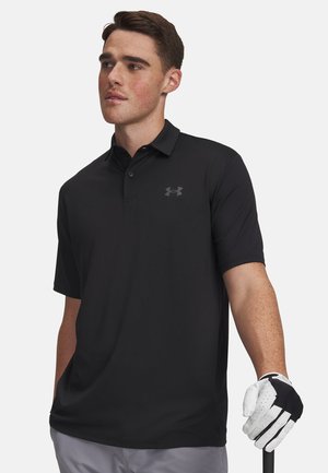 Junger Mann trägt ein schwarzes Poloshirt und einen weißen Golfhandschuh, hält einen Golfschläger und schaut leicht zur Seite vor einem schlichten Hintergrund.