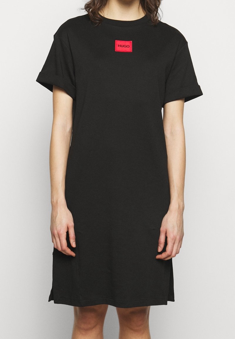 Robe t-shirt en coton noir dotée d'un col rond, de manches courtes retroussées, et d'un patch logo rectangulaire rouge sur la poitrine.