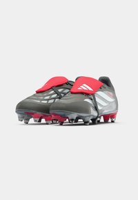 Botas de fútbol en gris con acentos rojos. Presentan una parte superior texturizada, un diseño elegante y correas negras, con tacos visibles en la suela.