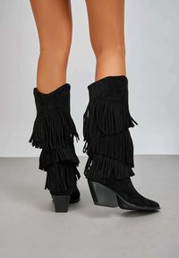 Bottes de cowboy en suède noir avec plusieurs couches de franges, bouts pointus et talon empilé. Texture lisse avec une finition mate.