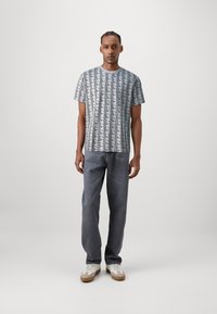 Short-sleeve, geometric patterned shirt in light gray and black, paired with loose gray jeans and white sneakers with brown accents.