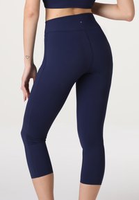 Leggings attivi blu navy con vita alta, realizzati in tessuto elasticizzato. Presentano dettagli delle cuciture e un design cropped e aderente.