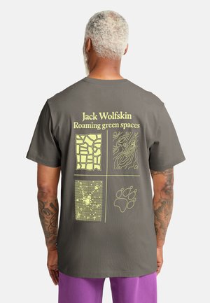 Maglietta grigia in cotone con quattro disegni grafici gialli sul retro, tra cui mappe, trame e un'impronta di zampa. Visualizza in modo prominente il nome del marchio.