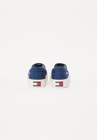 Zapatillas de lona azul marino con diseño de corte bajo, suelas de goma beige y una marca en el talón que presenta acentos en rojo, blanco y azul.