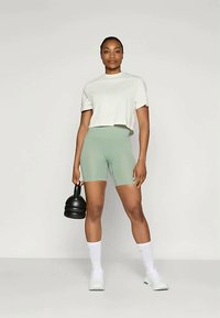 Šviesiai pilkas trumpas marškinėliai ir griūvos mėtų žalios spalvos dviratininkų šortai. Modelis laiko juodą kettlebell'ą. Išbaigtą įvaizdį papildo baltos kojinės ir sportbačiai.