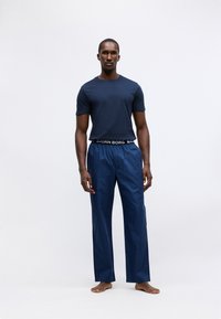 Navy plava majica kratkih rukava u kombinaciji s prugastim navy hlačama koje imaju crni pojas s logom "BJORN BORG". Model stoji bos.