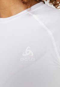 White athletic shirt with a smooth texture, featuring a subtle logo and reinforced seams. Noticeable horizontal pattern accents.