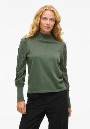 Groene trui met een hoge hals en gestructureerde, geprinte mouwen. Het lichaam is glad, terwijl de mouwen een ruitpatroon hebben.
