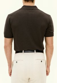 Brun kortärmad poloskjorta med mjuk textur. Stylerad med krämfärgade byxor med bakfickor och ett svart bälte.