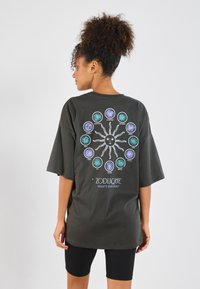 Dark gray oversized t-shirt featuring a sun graphic and zodiac symbols in various colors on the back. Short sleeves, relaxed fit.