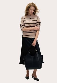 Svart läderhandväska med vid öppning, stadiga handtag och gulddetaljer, kombinerad med en randig tröja och en svart kjol. Platta skor.