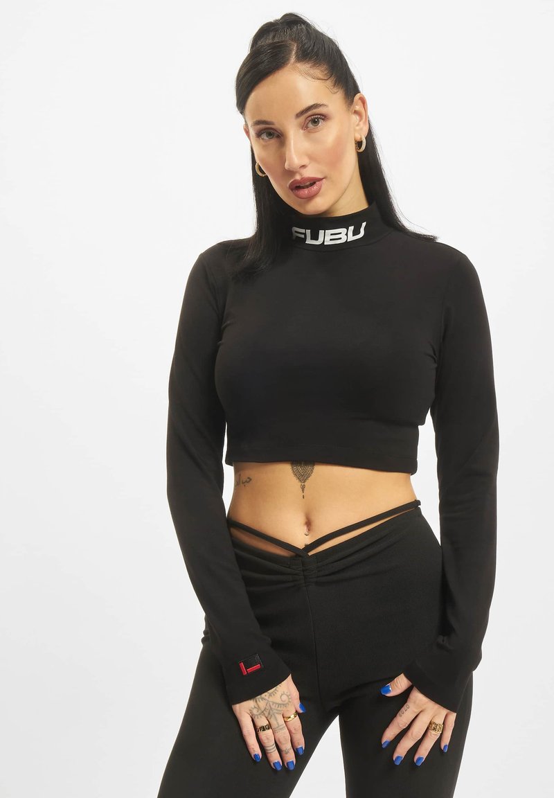 Čierny crop top s dlhými rukávmi a vysokým výstrihom, na ktorom sa nachádza biele logo "FUBU". Materiál je hladký, nosený s vyhovujúcimi čiernymi nohavicami.