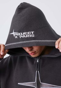 Sudadera con capucha de tejido gris oscuro, con el logotipo bordado "PROJECT X PARIS". Diseño sencillo con cierre de cremallera y costuras en contraste.