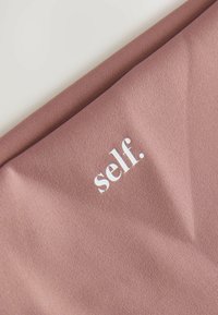 Mauve kangas, millel on sujuv tekstuur ja silmapaistvalt valge trükitud logo "self." paigutatud diagonaalis.