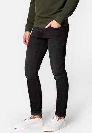 Czarne dopasowane jeansy z denimu, o gładkiej fakturze, subtelnych detalach przeszyć i zwężanym kroju nogawki, w zestawie z białymi sneakersami.