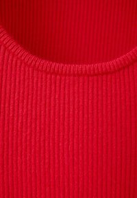 Gros plan sur un tissu tricoté côtelé rouge avec un col arrondi montrant la texture et les détails des coutures.
