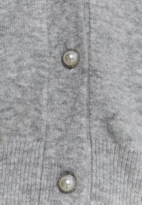 Graue Strickjacke mit weicher Textur, ausgestattet mit runden, perlenähnlichen Knöpfen und gerippten Details entlang der Kanten.