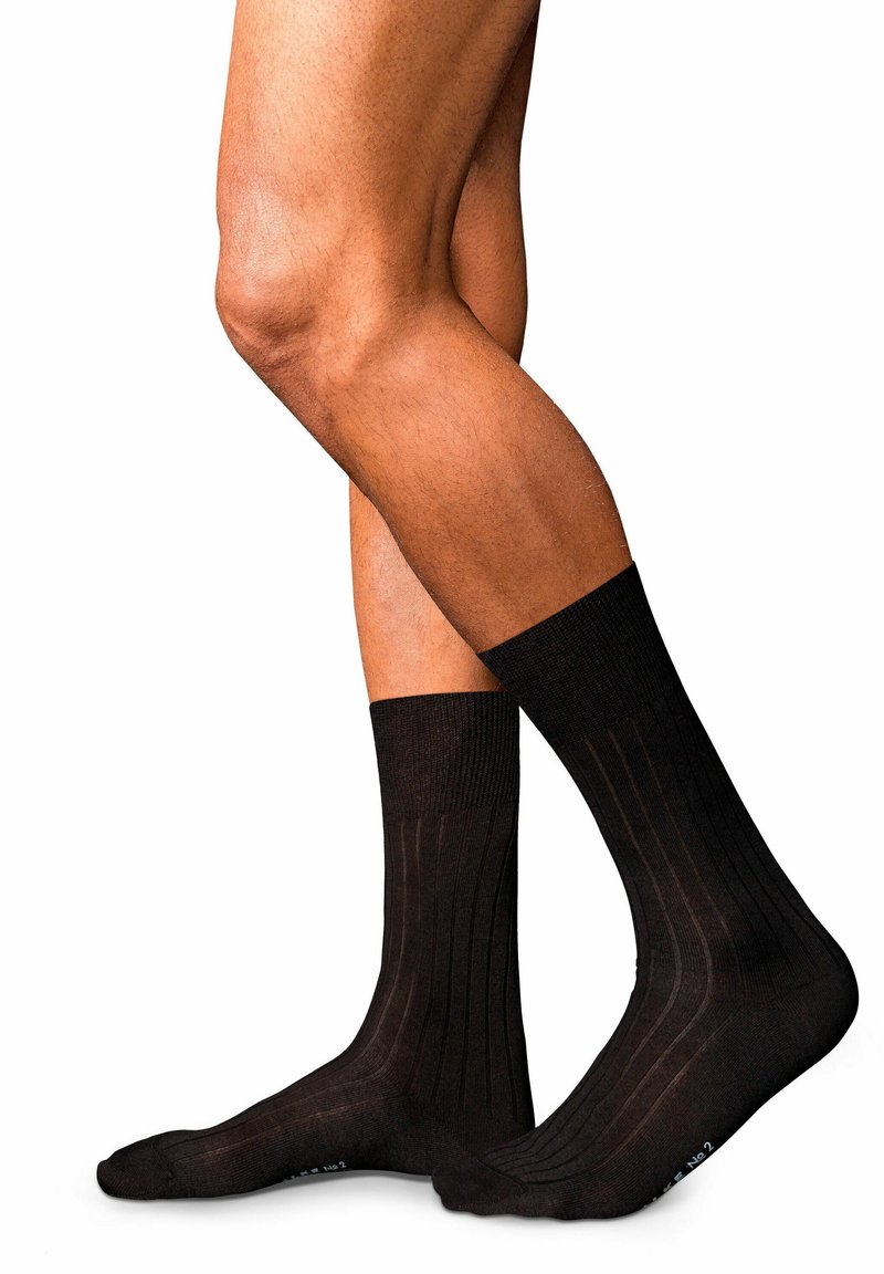 Calzini neri in cotone a coste con punta senza cuciture, dotati di un polsino rinforzato e una texture sottile, posizionati su gambe con uno sfondo neutro.