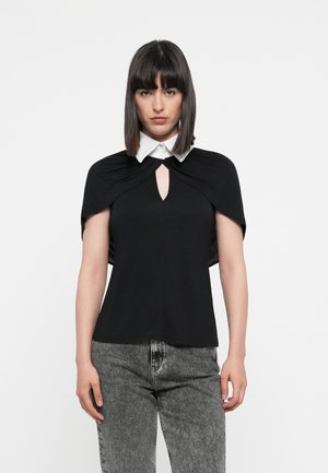 Black top with short, draped sleeves, a white collar, and a keyhole neckline. Worn with gray, high-waisted jeans. Smooth texture throughout.