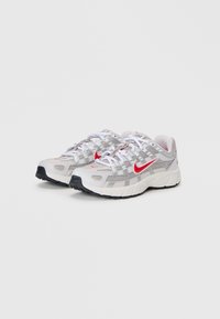 Nike tenisice za trčanje s gornjim dijelom od sive mrežice, crvenim logotipom, bijelim vezicama i crnim potplatom. Dizajn uključuje ventilacijske rupe i strukturirane akcentne detalje.