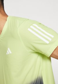 Camiseta deportiva verde claro con textura de malla, diseño de cuello en V y logo blanco de tres rayas en el hombro. Diseño en degradado cerca del dobladillo.