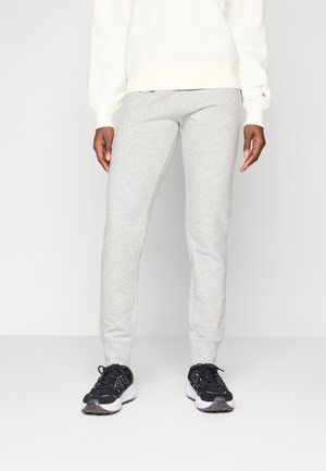 Grå joggebukser laget av mykt materiale med en tettsittende design. Kombinert med svarte sneakers med hvit såle og teksturerte detaljer.