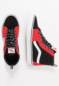 Baskets montantes avec un extérieur en daim noir et rouge, des accents latéraux blancs, des lacets gris et une semelle en caoutchouc blanche.