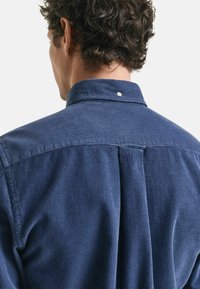 Navyblaue Cordhemd mit Knopfkragen, ausgestattet mit einer vertikalen Falte auf dem Rücken und geripptem Textil. Schlichte Ausführung ohne Muster.