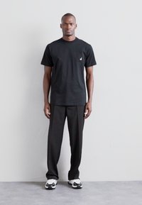 Must musta T-särk lühikeste varrukatega, mille vasakul rinnal on väike valge logo, kombineeritud lõtvade mustade pükstega ja must-valgete tossudega.