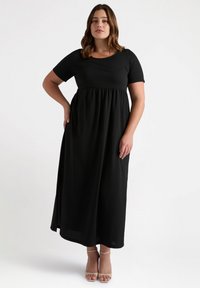 Black maxi dress with short sleeves, rounded neckline, and elastic waist. Flowing fabric with a smooth texture and side slit.