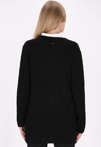 Schwarzer Strickpullover mit Zopfmuster, langen Ärmeln und lässiger Passform, der eine strukturierte Oberfläche in einer einfarbigen Ausführung zeigt.