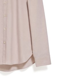 Camicia button-up beige chiaro, maniche lunghe, tessuto morbido, orlo arrotondato, presenta cinque bottoni, con una sottile texture e cuciture pulite.