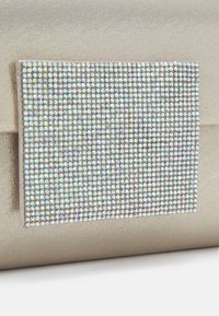 Kabelka na clutch v béžovém saténu s obdélníkovou ozdobou z křišťálů, na které jsou uspořádány mnohé iridescentní kameny ve tvaru mřížky.