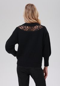 Czarny sweter z teksturowanym trójdzielnym ciałem i koronkowym panelem z tyłu. Posiada opadające ramiona i ściągacze przy mankietach.