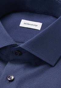 Marineblauw geweven overhemd met een visgraatpatroon, een button-down kraag en een label met de tekst "seidensticker." Matte zwarte knopen.