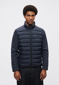 Marineblå dunjakke med høj krave, quiltet front og glatte ærmer. Har lynlås foran og sidelommer.