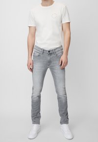 Jeans in denim grigio con una vestibilità slim, dotati di tasche anteriori e posteriori, leggera scoloritura e chiusura con bottone nero. Abbinati a una t-shirt bianca.