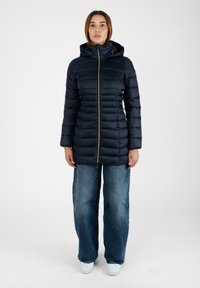 Giacca in nylon imbottita di colore blu navy con un design aderente, cappuccio e zip a contrasto. Indossata su jeans azzurri a gamba larga e sneakers bianche.