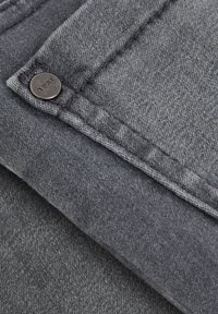 Tejido de denim gris oscuro con un botón grabado con la palabra "next", textura sutil y costuras contrastantes a lo largo del dobladillo.