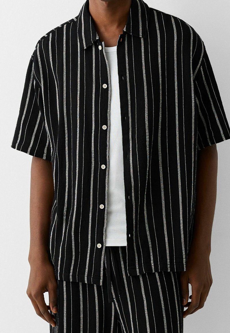 Black and white vertically striped short-sleeve shirt with a button-up front and a textured fabric, paired with matching bottoms.