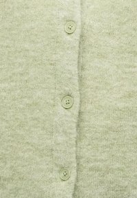 Lysegrønn strikket stoff med en rad av tre små, runde, firehulls knapper sydd vertikalt ned midten.