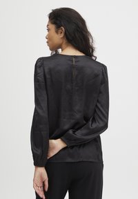 Schwarze Satinbluse mit Puffärmeln, geraffter Taille und Knopfverschluss hinten. Glatte Textur und elegantes Design.