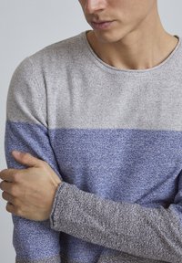 Prugasta dolga majica s dolgimi rokavi v svetlo sivi in modri barvi. Mehak, teksturen material z rebrastimi manšetami. Oblikovanje s krožnim ovratnikom, prilagojeno okoli trupa.